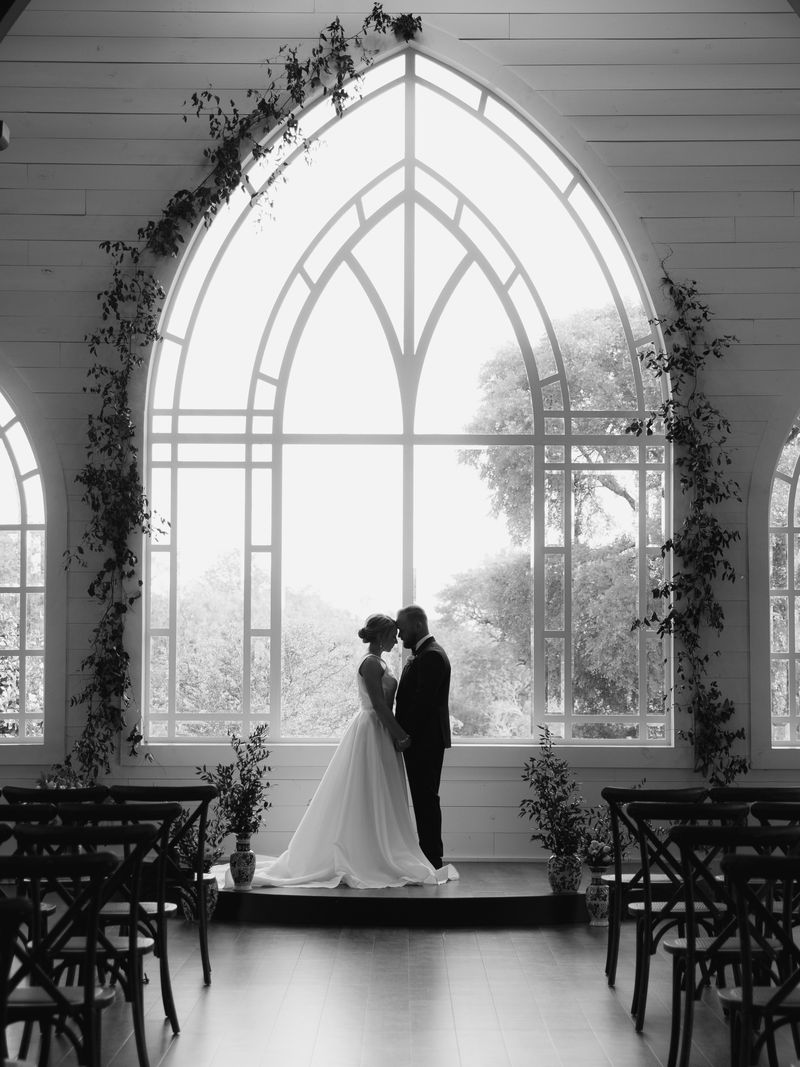 Bride and groom silhouetted before the arched chapel window